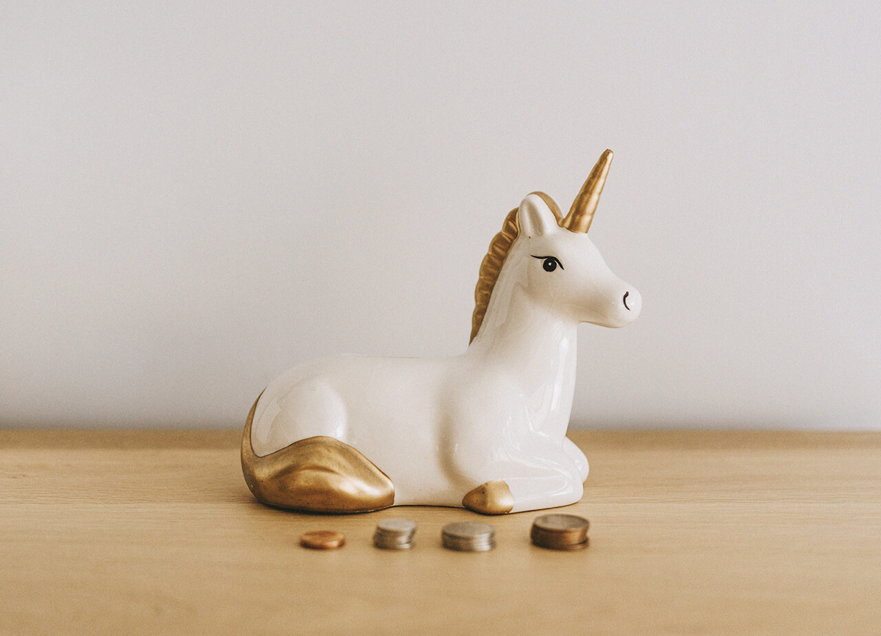 A white and gold ceramic unicorn on table in front of piles of coins.