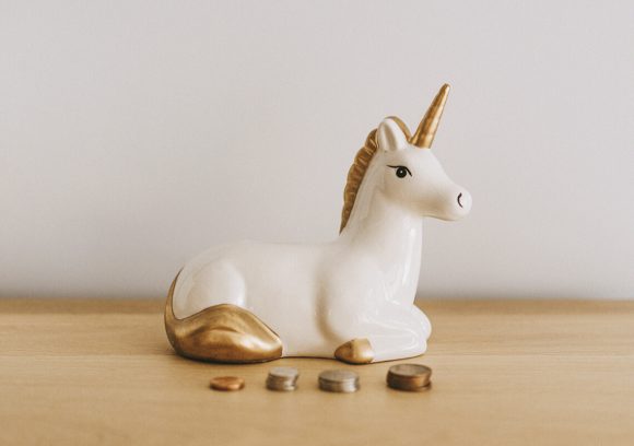 A white and gold ceramic unicorn on table in front of piles of coins.