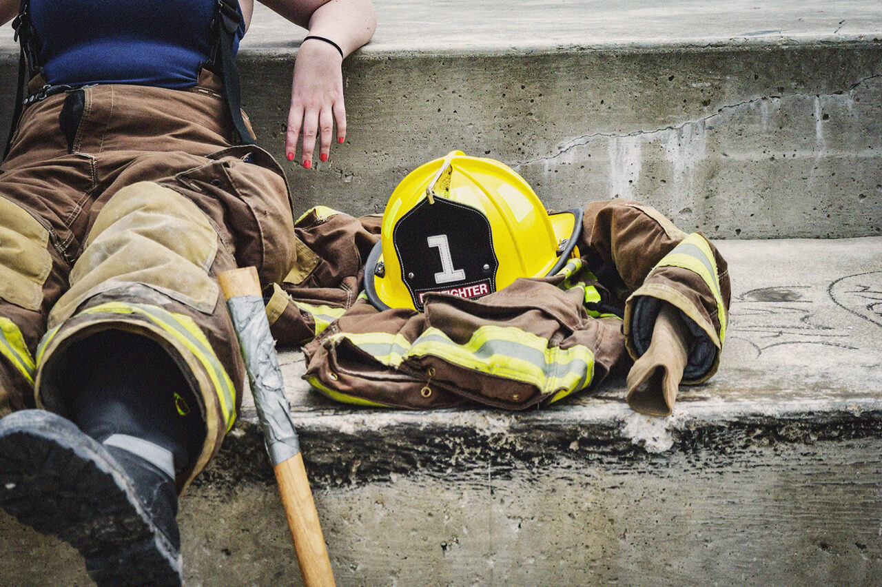 Firefighter seated on concrete steps next to their helmet and jacket. Close-up.