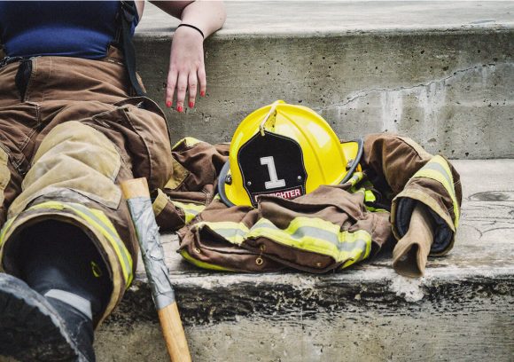 Firefighter seated on concrete steps next to their helmet and jacket. Close-up.