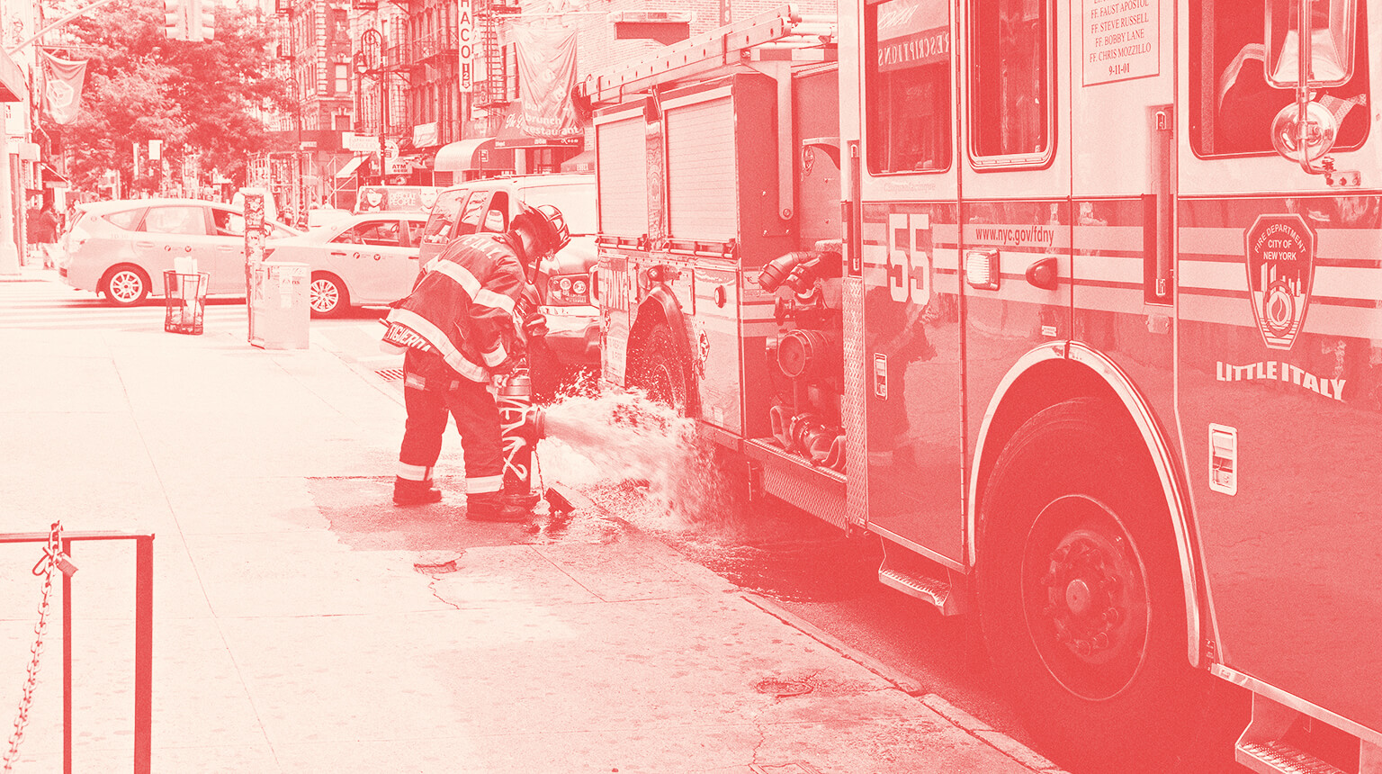 Firefighter standing next to a firetruck while monitoring an open fire hydrant.