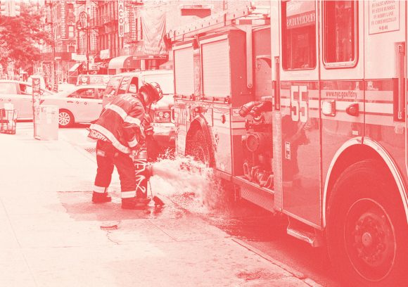 Firefighter standing next to a firetruck while monitoring an open fire hydrant.