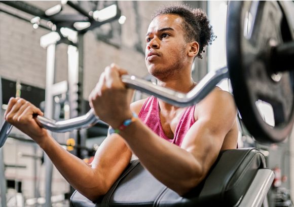 Person at a gym using a curl bar while seated.