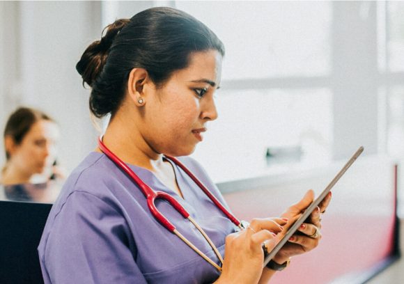 Nurse wearing a stethoscope review information on a tablet.