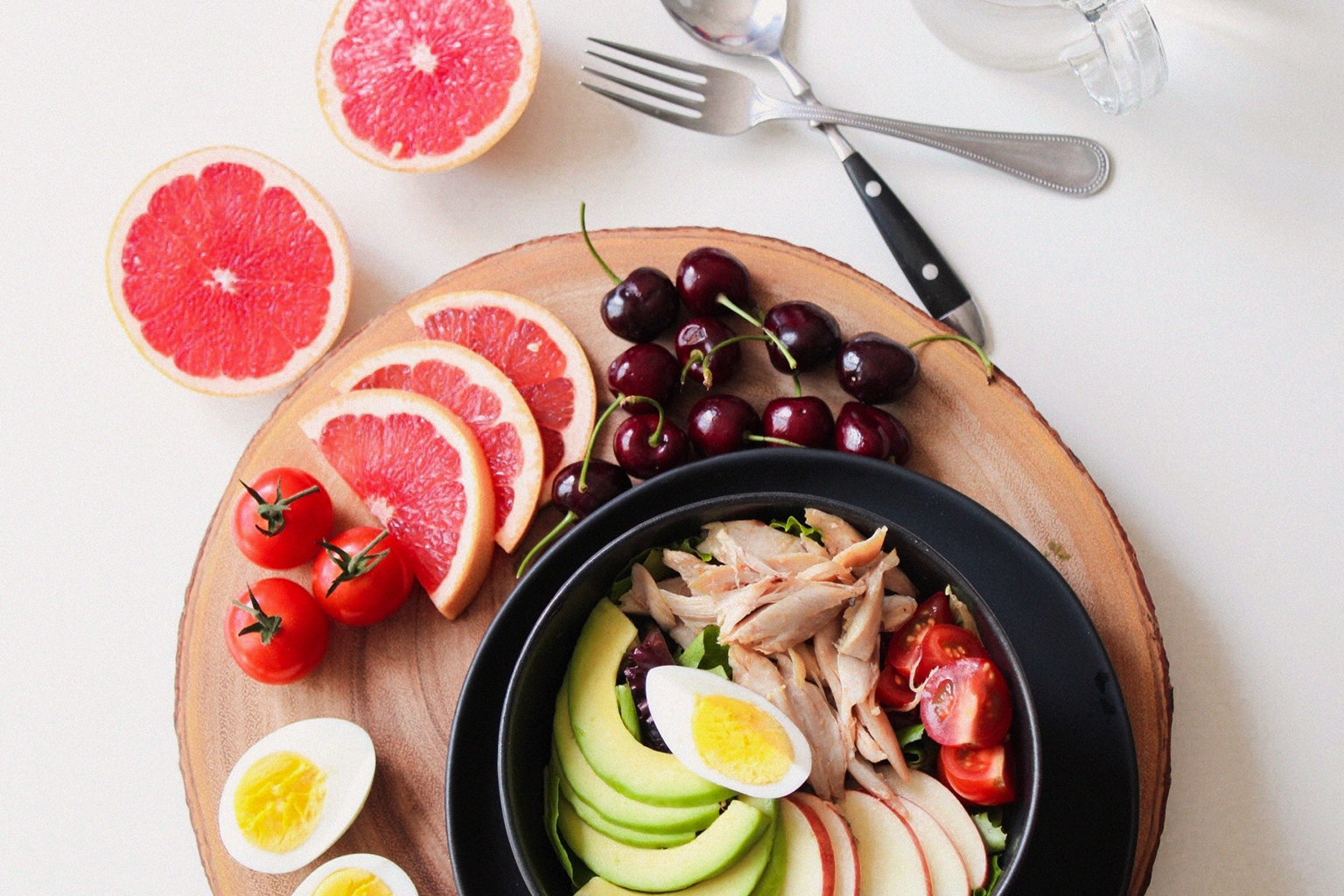 Top-down view of a healthy salad featuring avocado, grapefruit, cherries, and hard-boiled egg.