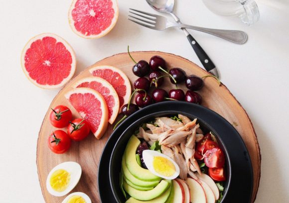 Top-down view of a healthy salad featuring avocado, grapefruit, cherries, and hard-boiled egg.