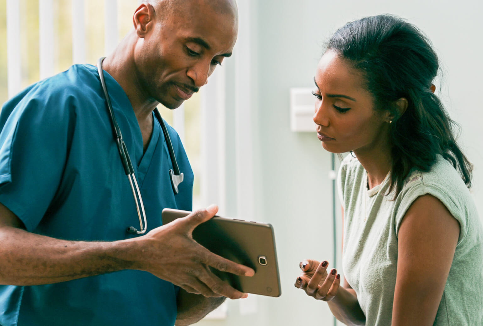 A CNA wearing a stethoscope shows a patient information on a tablet.