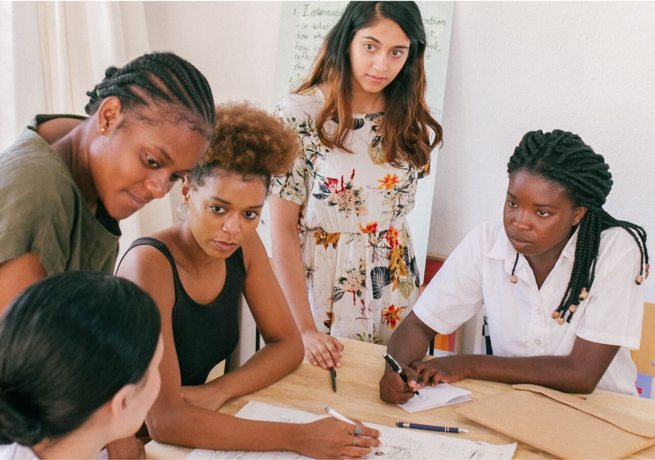 Group of people sitting around a table with pens and paper studying together.