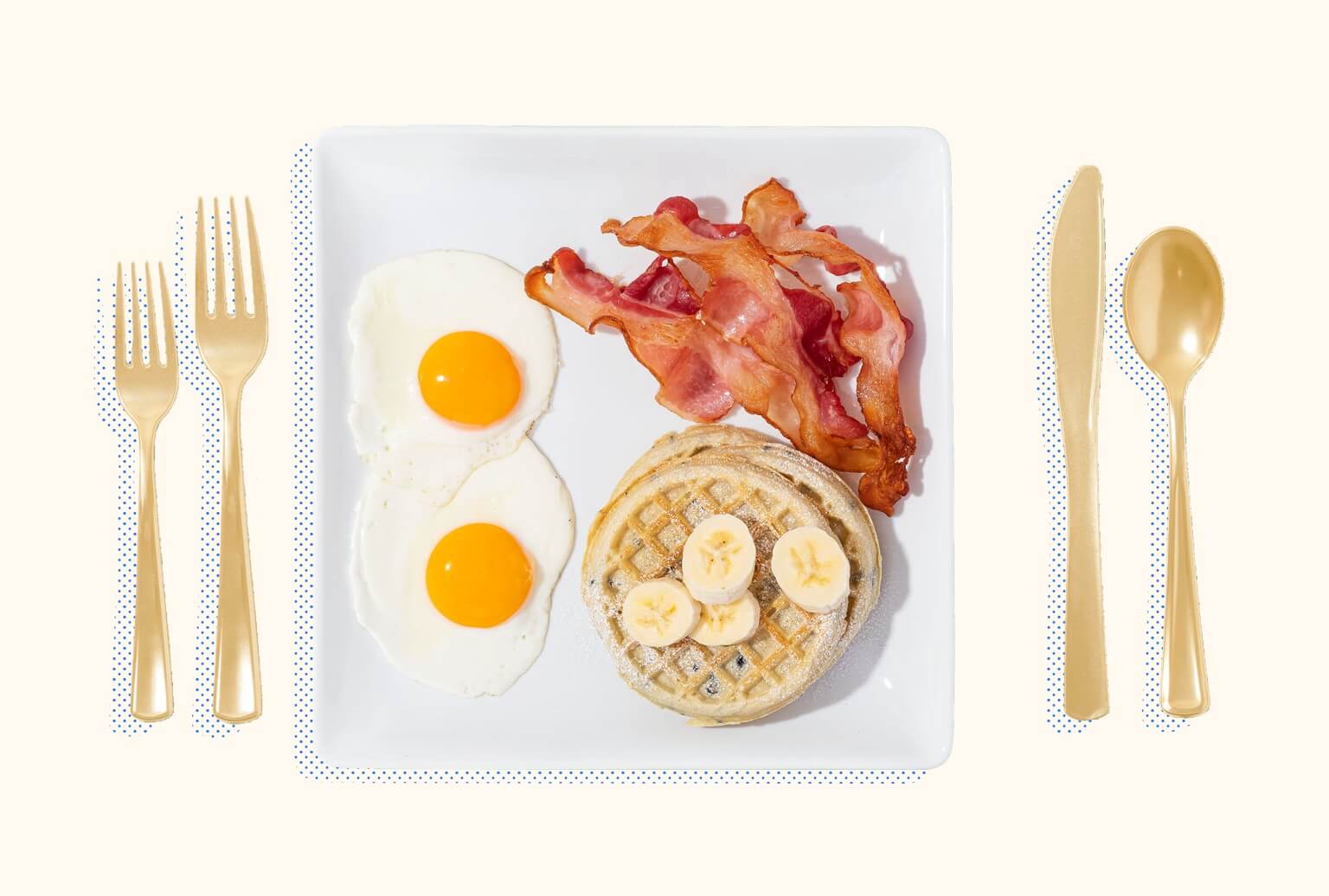 Bacon, eggs, waffles, and cut bananas on a square plate with silverware on either side.