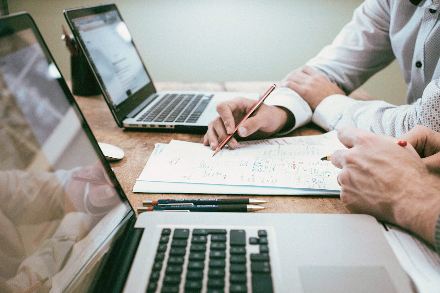 A certified financial planner reviews paperwork with a client at a table with laptops. Close up.