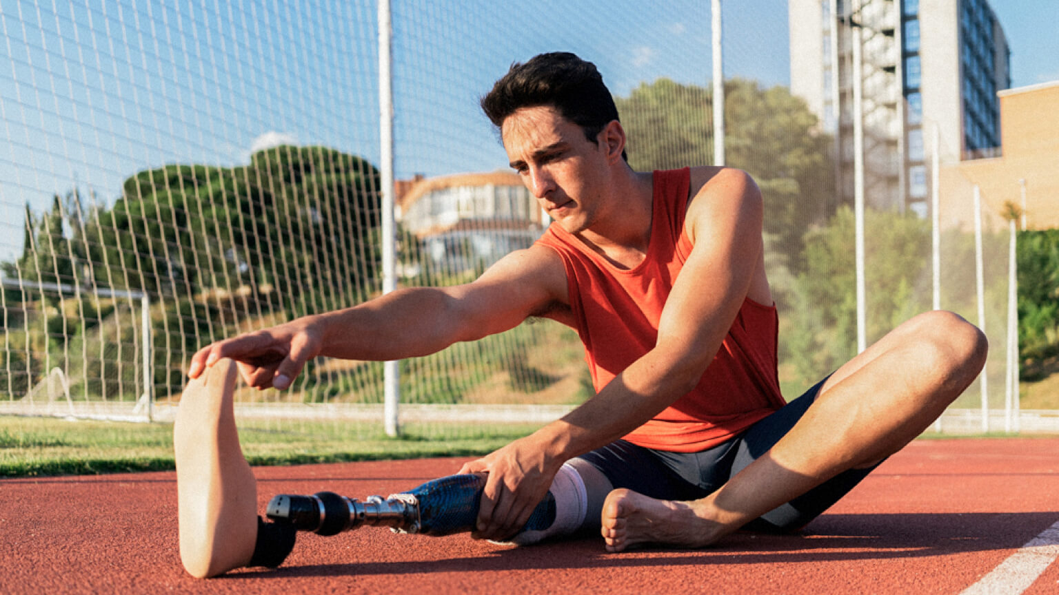 Person with prosthetic leg sitting on an outdoor track stretching.