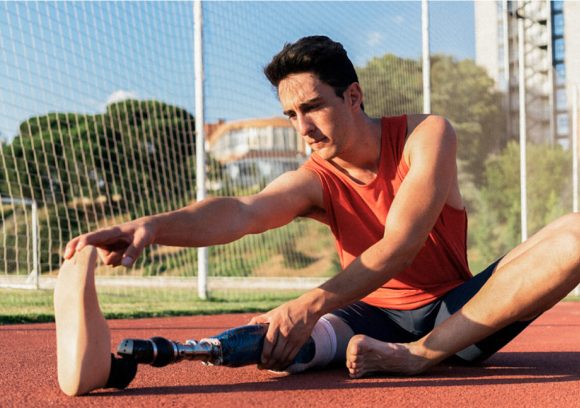 Person with prosthetic leg sitting on an outdoor track stretching.