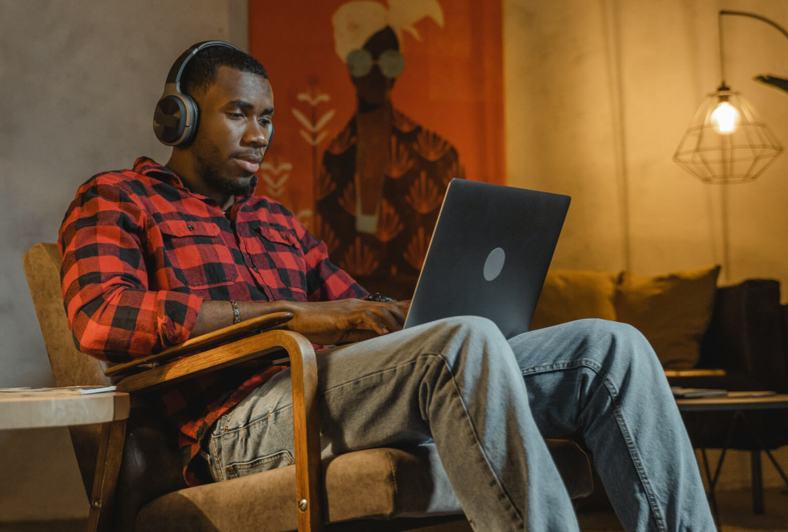 Person wearing wireless headphones sitting in a comfy chair while using a laptop.