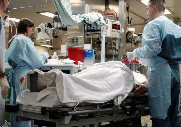 Two trauma nurses treat a patient lying on a gurney in a hospital.