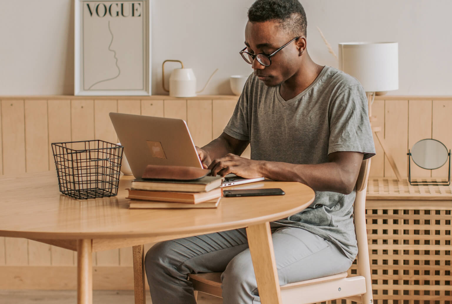 A person wearing glasses working at a laptop on a table with books.