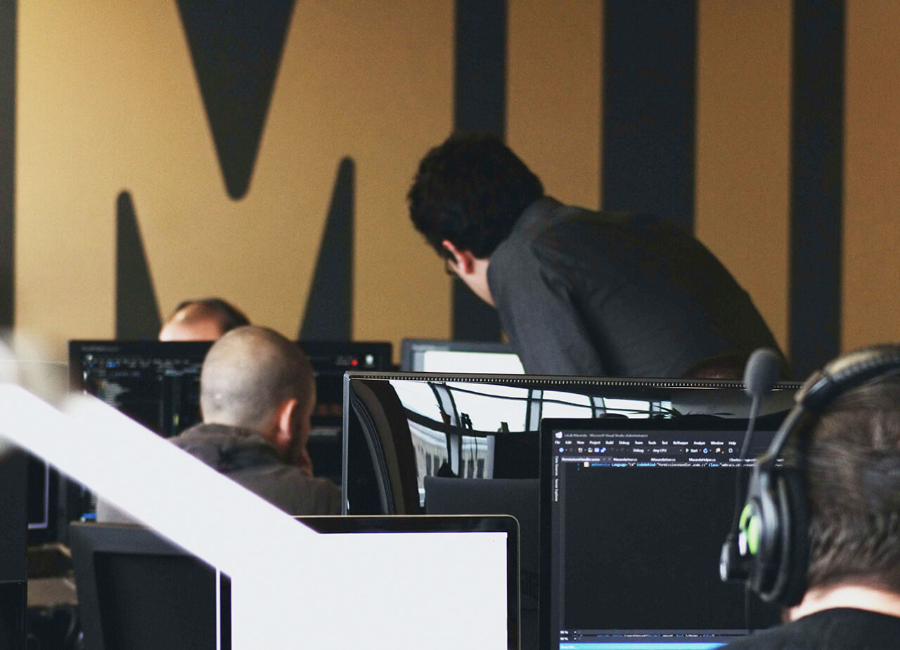 A cybersecurity professional looks at a coworker's computer screen in an office.