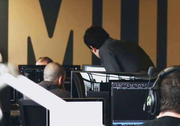 A cybersecurity professional looks at a coworker's computer screen in an office.