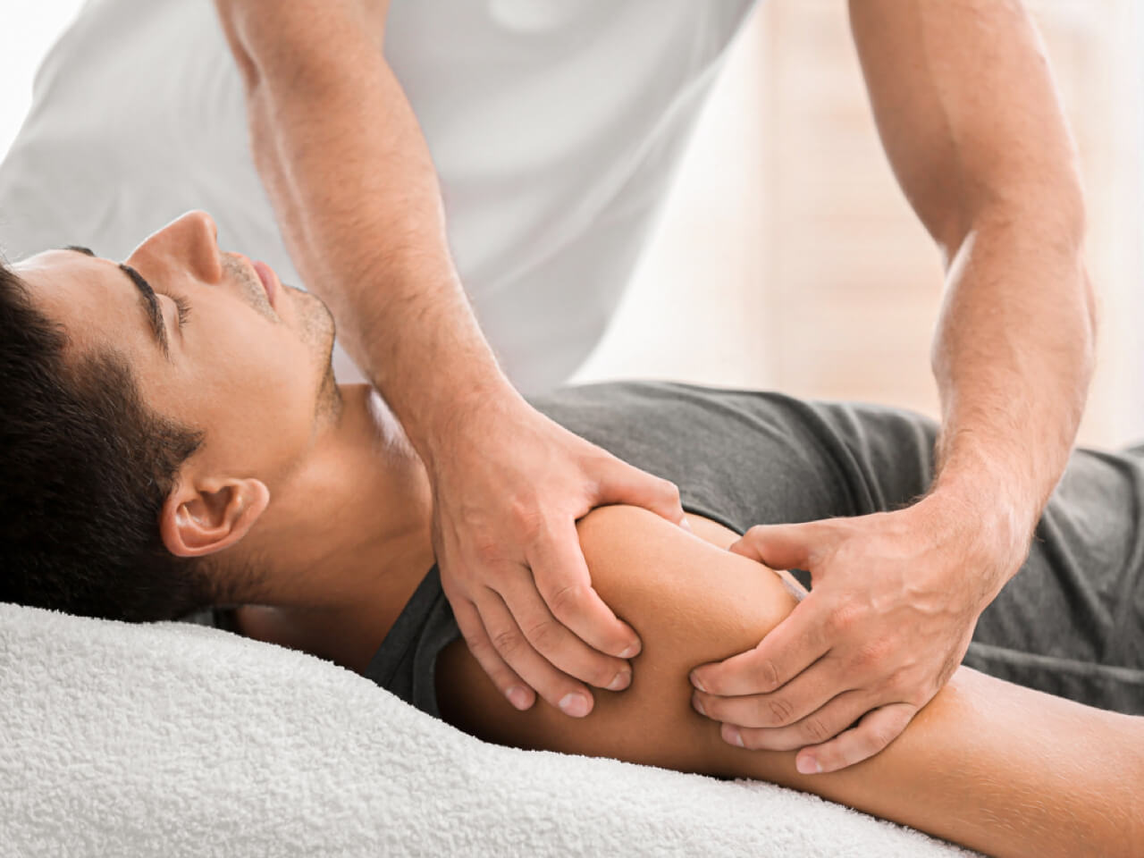 Person getting massage work done on their shoulder while lying on a table.