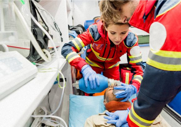 Two paramedics performing CPR on a patient inside an ambulance.