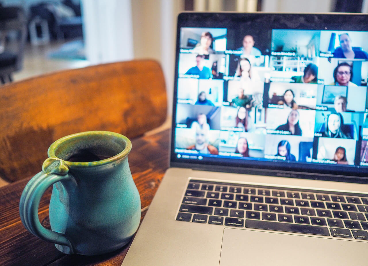 Coffee mug is sitting next to a computer showing a virtual meeting with multiple participants.