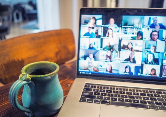 Coffee mug is sitting next to a computer showing a virtual meeting with multiple participants.