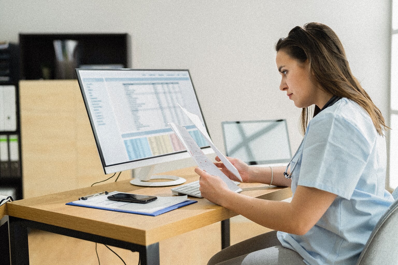 A certified medical coder sits a desk in front of a computer comparing paperwork.