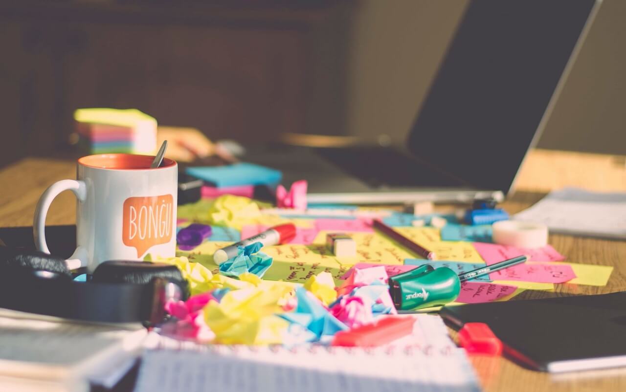 Cluttered desk with coffee mug, headphones, and lots of crumpled post-it notes.