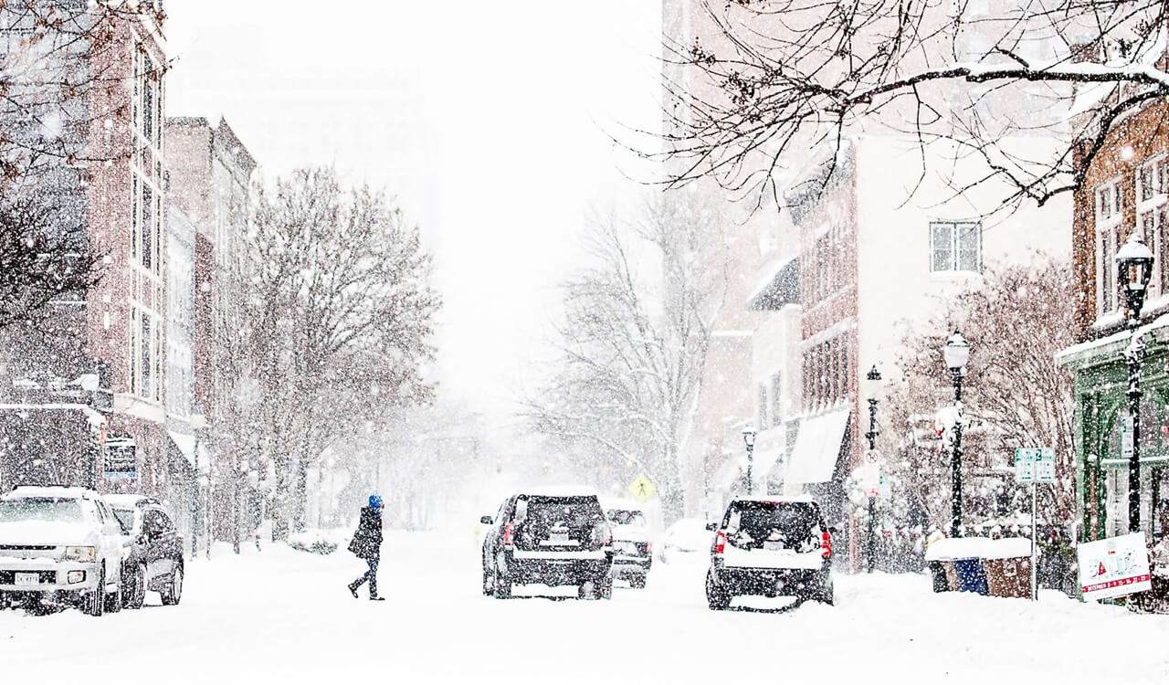 Person walking across a city street covered in snow during winter.