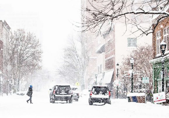 Person walking across a city street covered in snow during winter.