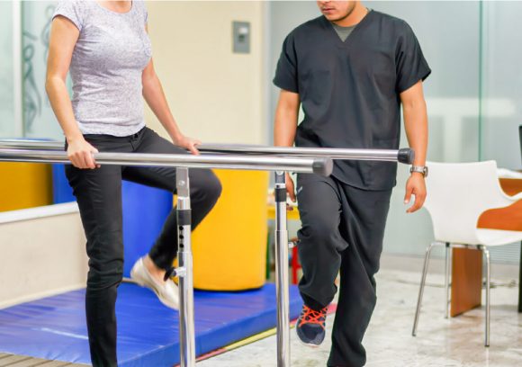 Occupational Therapist helping a patient on parallel rehabilitation bars.