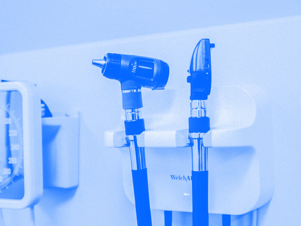 Two medical instruments hanging on a holder mounted to a wall. Blue-toned close up.