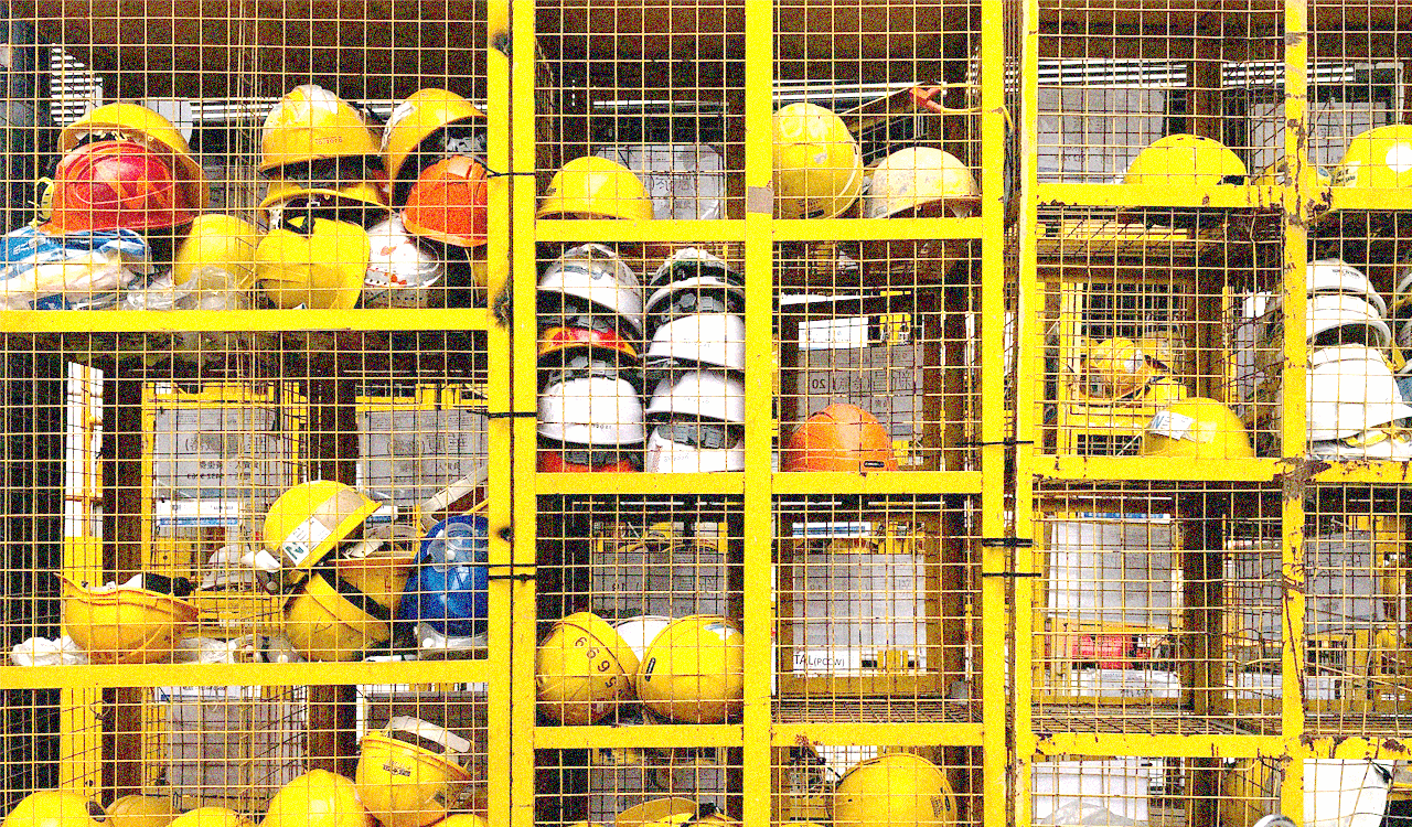 Multiple yellow hard hats stacked in a wire shelving unit.