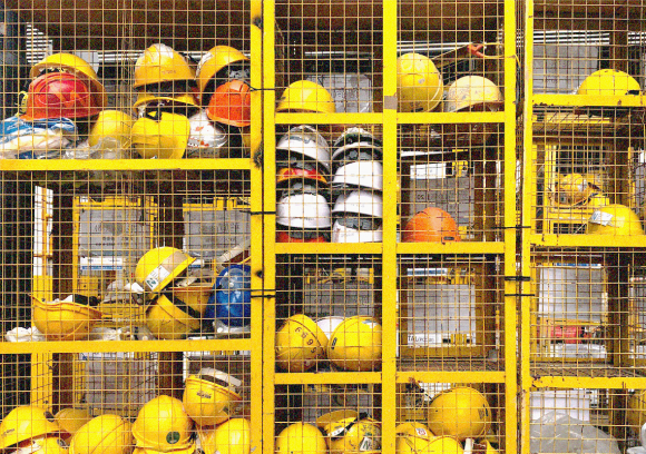 Multiple yellow hard hats stacked in a wire shelving unit.