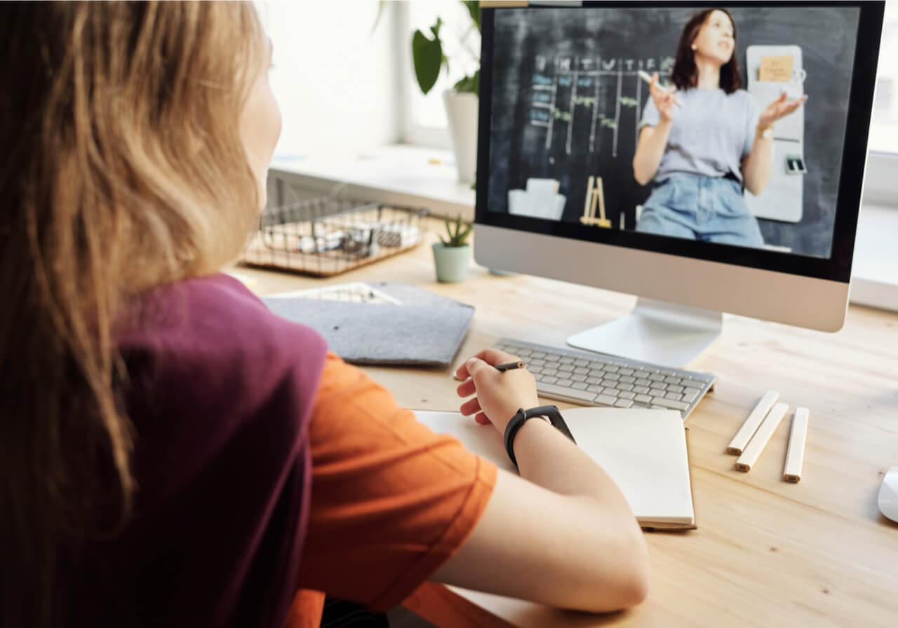 Person studying at a desk while watching an instructional video.