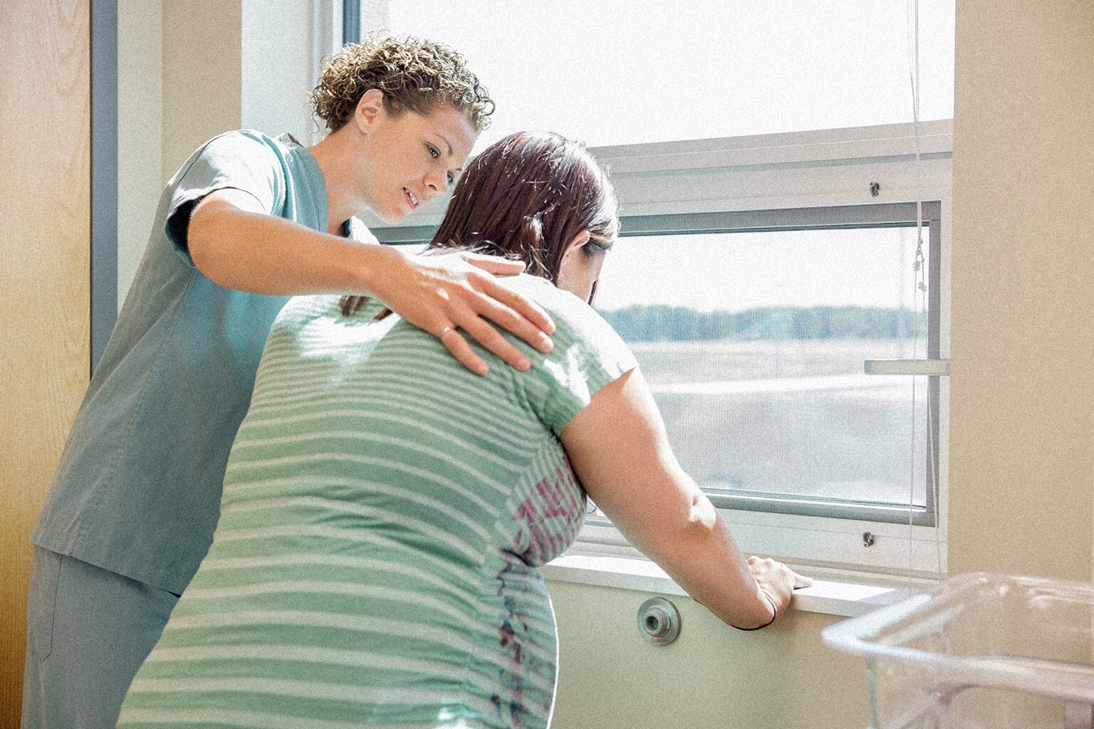 A midwife stands next to a patient at a window and helps her breath during labor contractions.