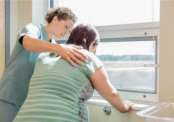 A midwife stands next to a patient at a window and helps her breath during labor contractions.