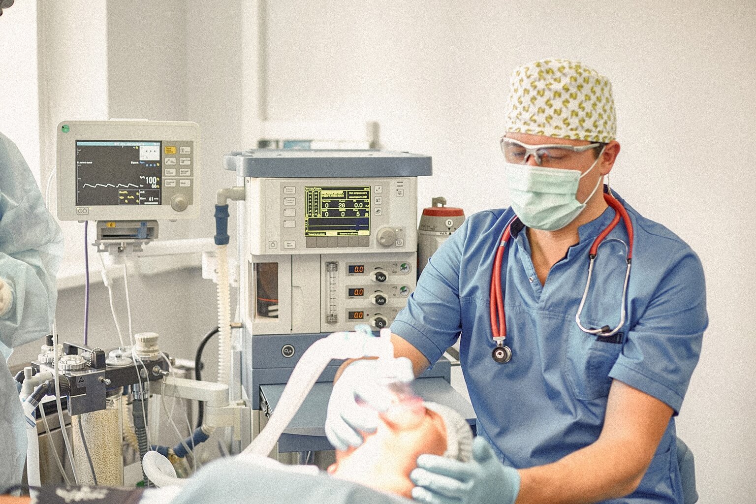 An anesthesiologist monitors an intubated patient in a hospital room.