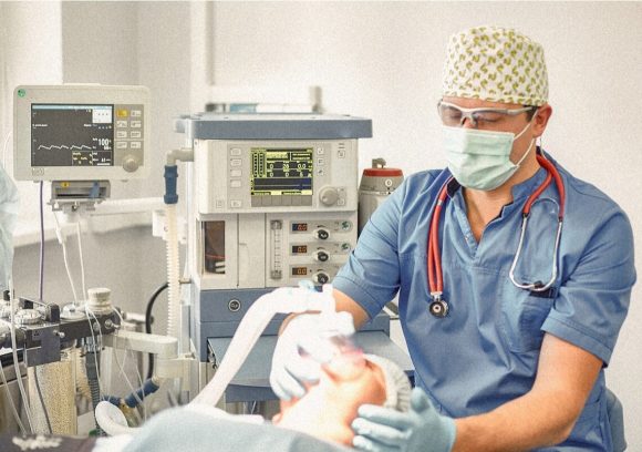 An anesthesiologist monitors an intubated patient in a hospital room.
