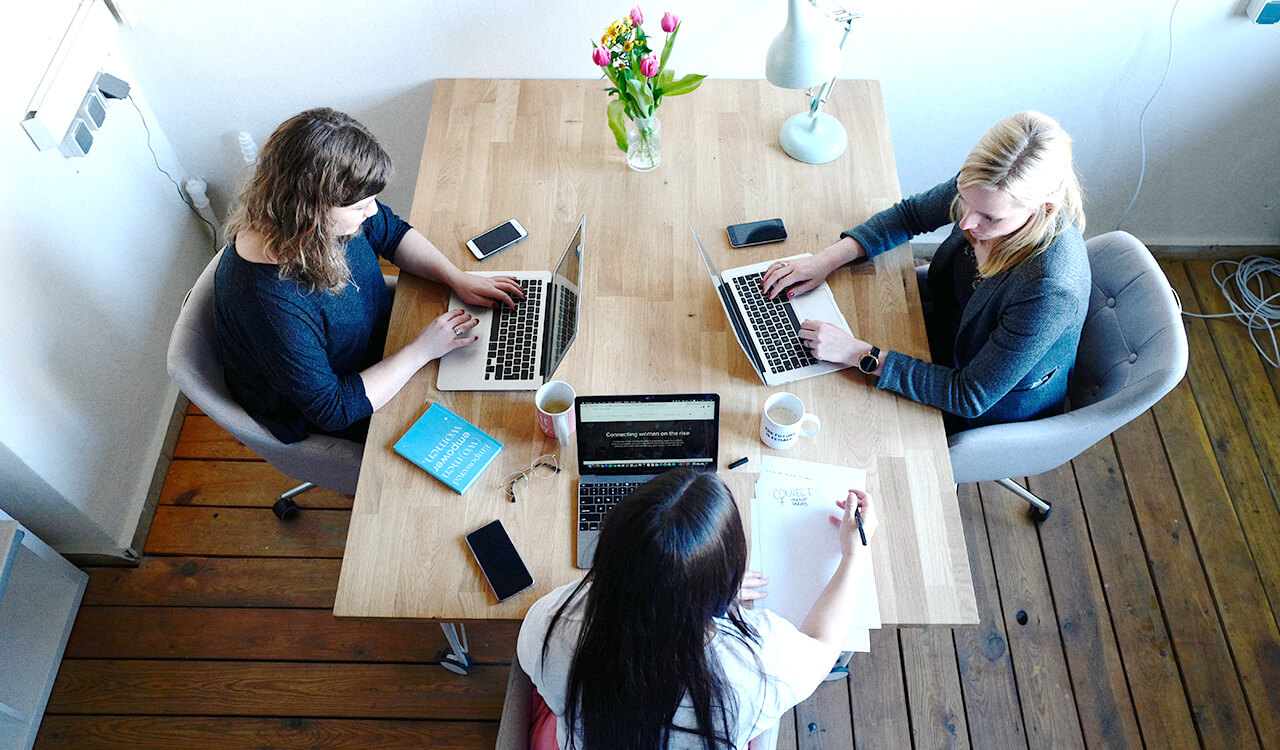 Three project managers sitting a table together while working on computers.