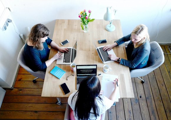 Three project managers sitting a table together while working on computers.