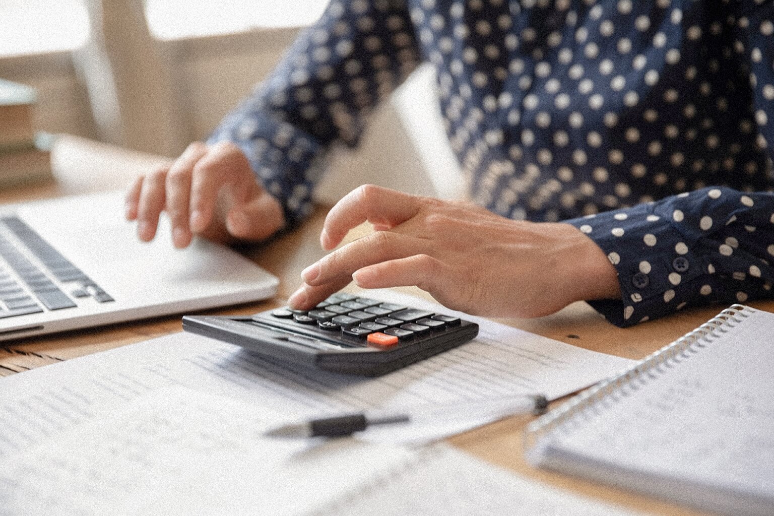 A person sitting at a desk with a computer while using a calculator. Close up.