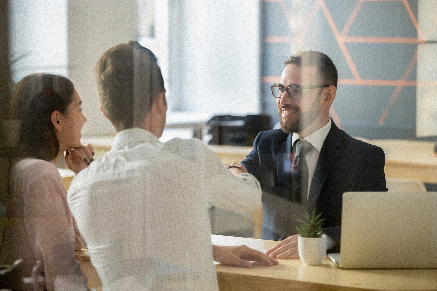 Two people meet with a certified financial planner at an office. One person is shaking the CFP's hand.