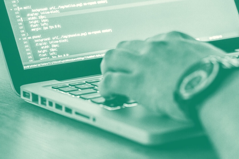 Image of a person's hand typing on a computer that shows lines of code. Close up. Tinted green.