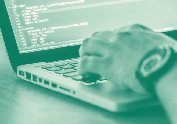 Image of a person's hand typing on a computer that shows lines of code. Close up. Tinted green.