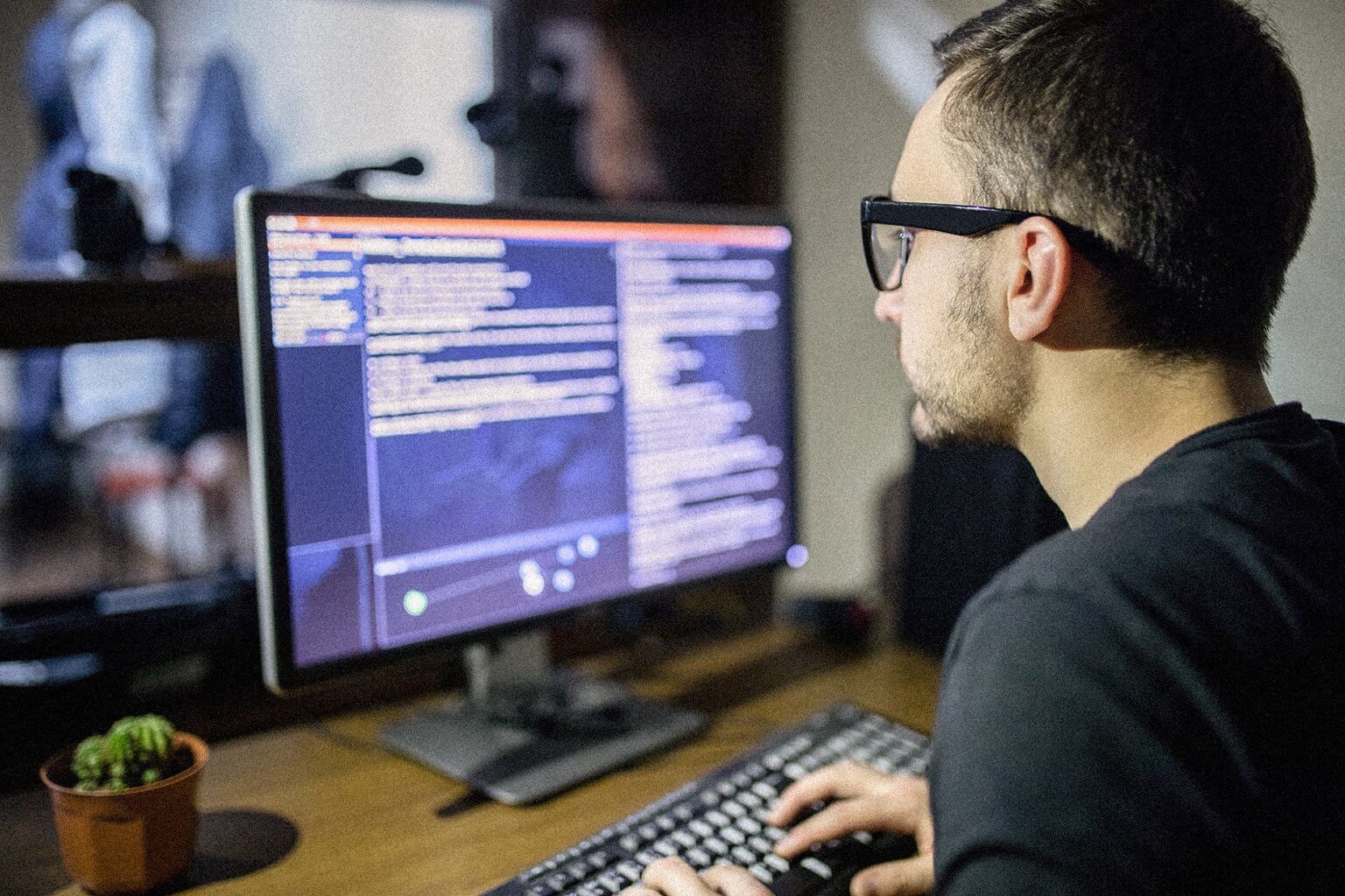 An IT professional sits at a desk with a computer while looking at lines of code.