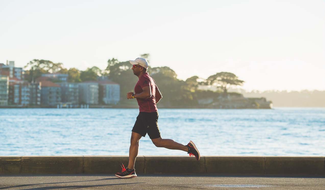 A person jogging on a road next to a large body of water.