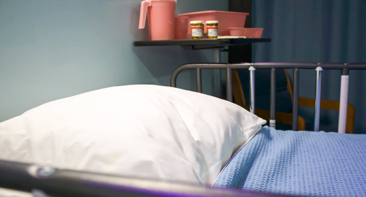 A hospital bed in front of a side table with medications and pink plastic containers.