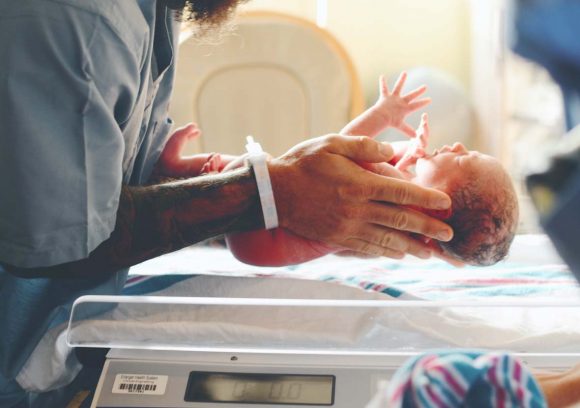 A neonatal nurse placing a newborn baby on a blanket in the hospital.