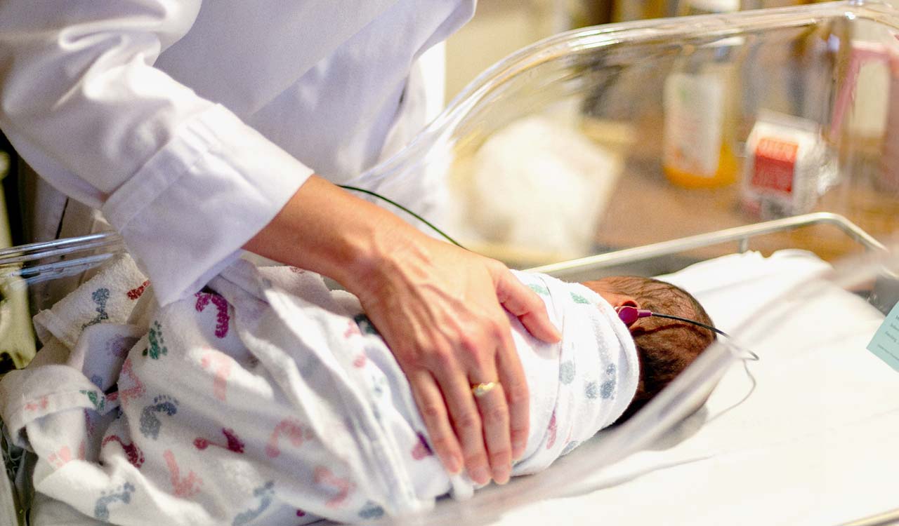 Neonatal nurse checking on a newborn baby in a hospital crib.