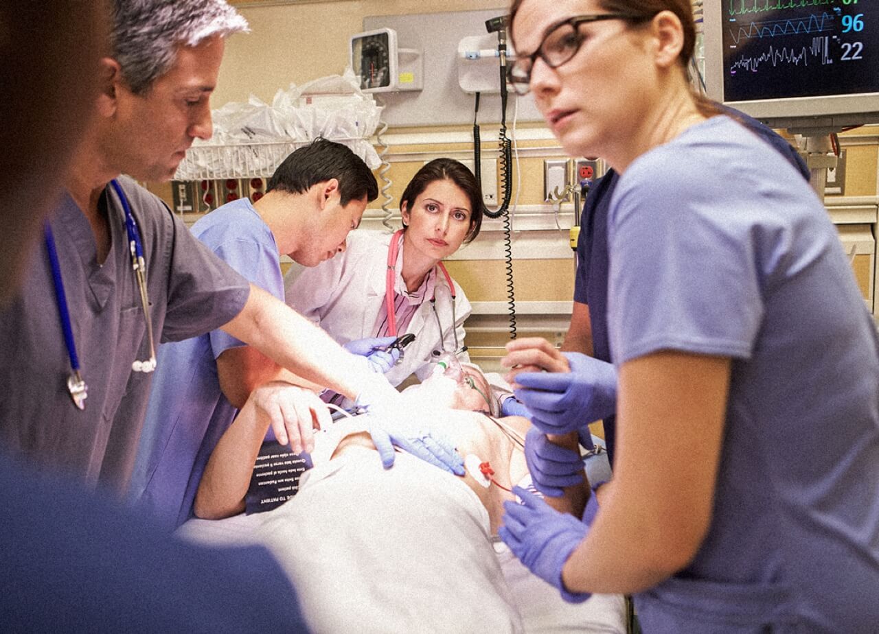 A group of emergency medical professionals work together over a patient in the ER.